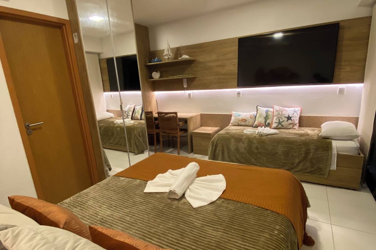 Moderni hotellihuone, jossa on suuri sänky, pienempi sänky, työpöytä ja televisio.