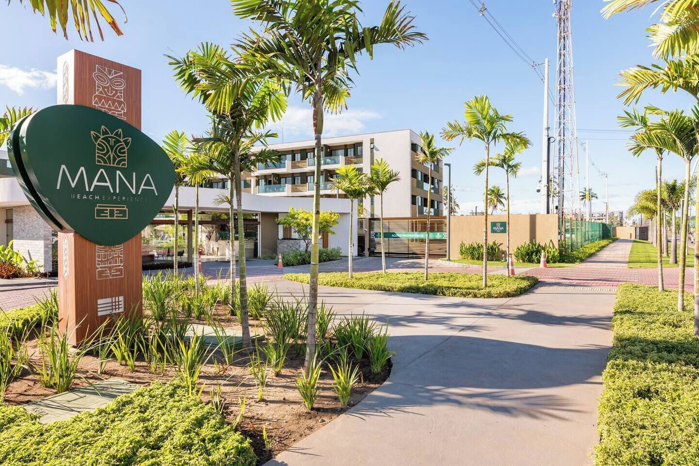 A modern hotel entrance with a sign reading "MANA BEACH EXPERIENCE" and a logo.
