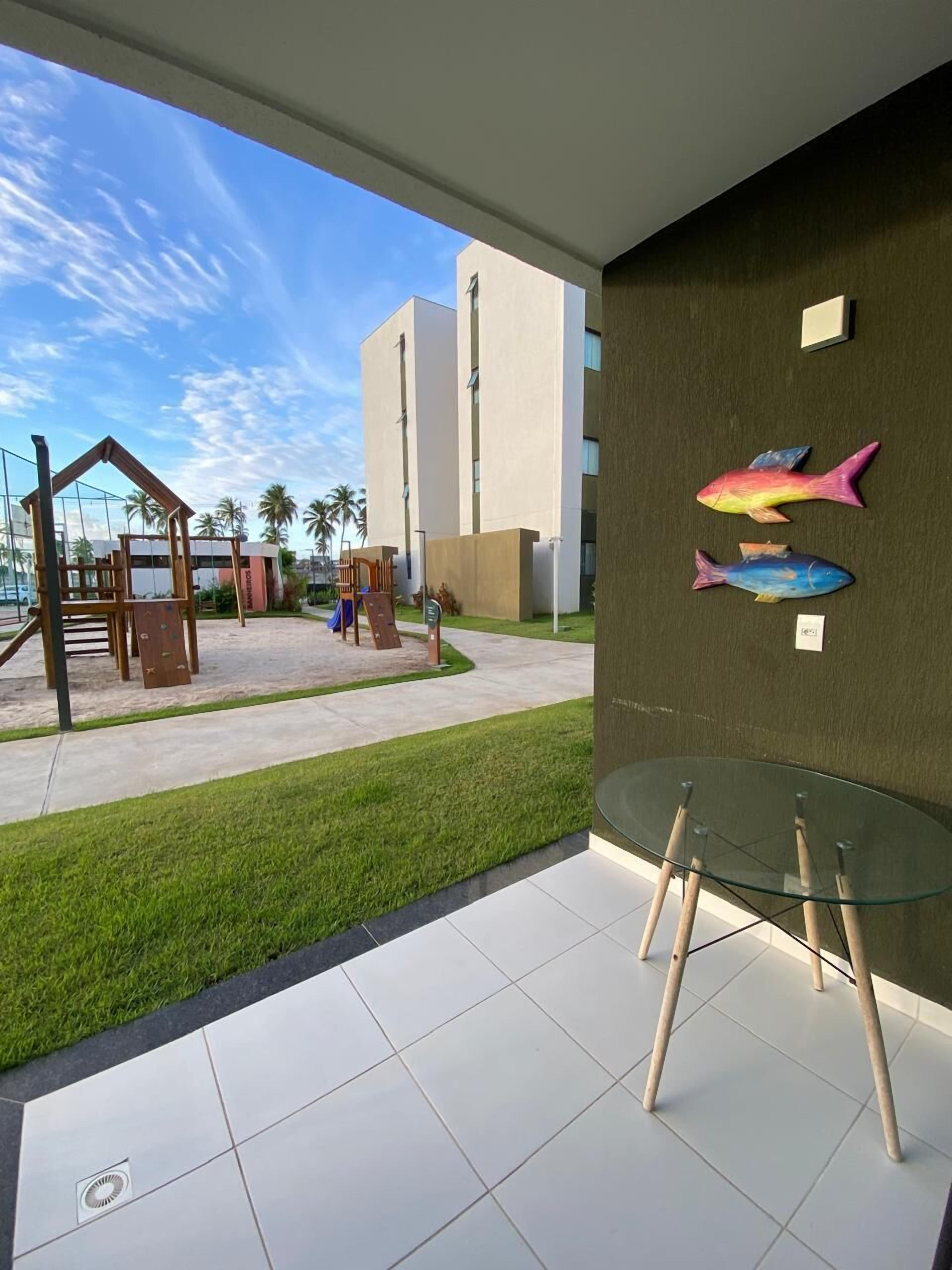 A modern building with a glass table and chairs, a grassy area, and two colorful fish decorations on the wall.