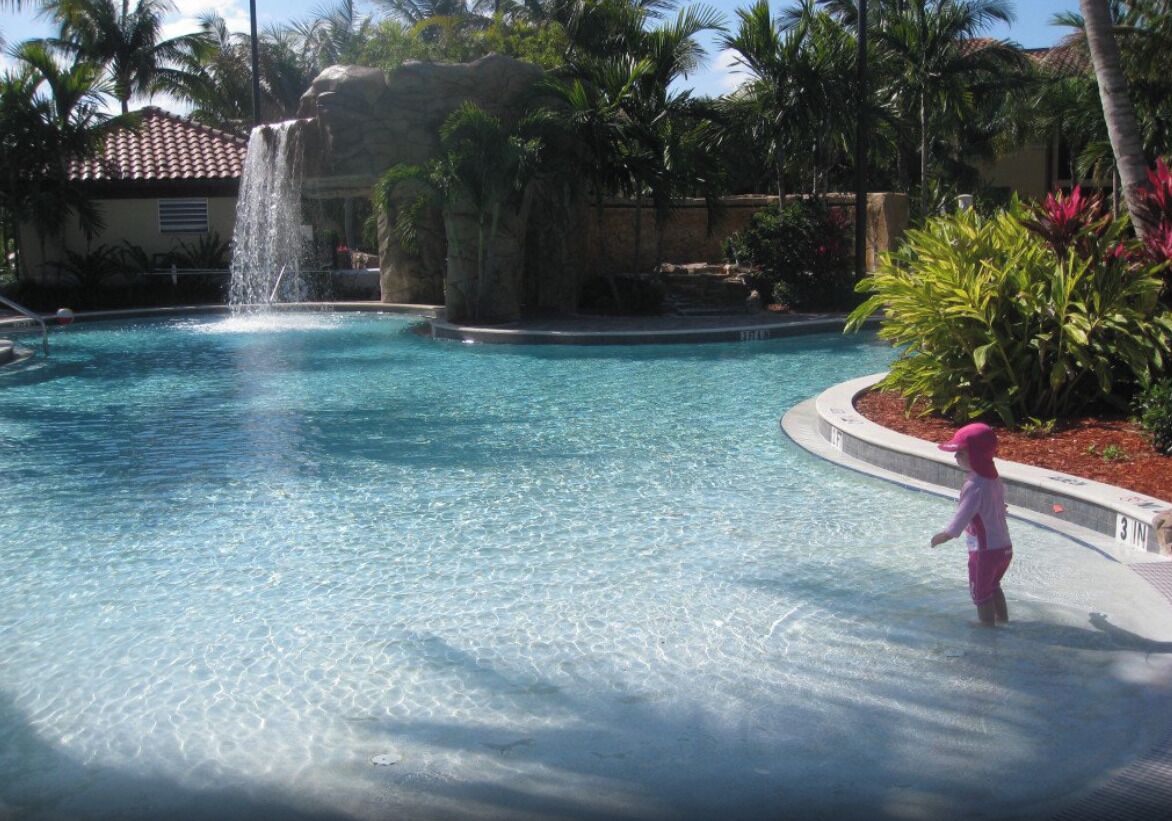 A clear pool with a waterfall feature, surrounded by palm trees and a small waterfall.
