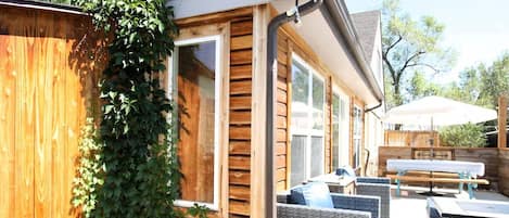 A wooden exterior wall with a window, a covered outdoor seating area with wicker furniture, and a wooden fence partially covered by ivy.