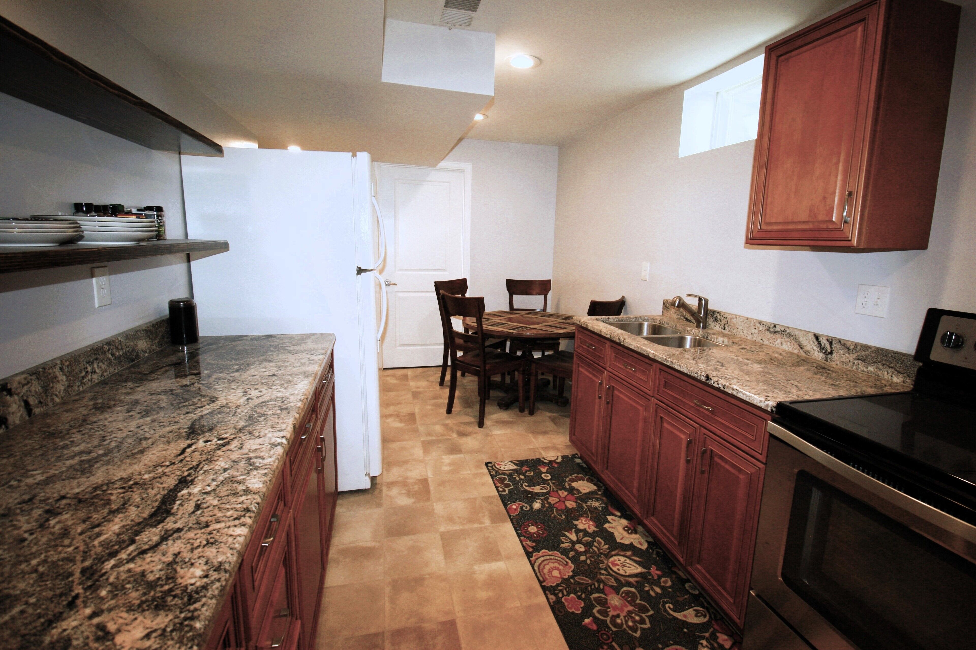 A kitchen with granite countertops, wooden cabinets, a built-in oven, and a dining area with chairs and a table.