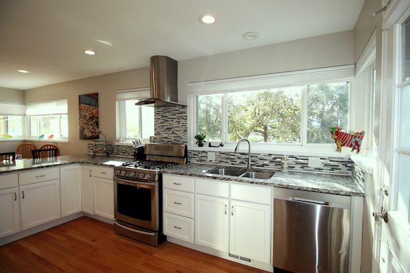 A modern kitchen with white cabinets, stainless steel appliances, and a large window providing a view of trees.