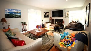 Un salon comprenant un canapé, un fauteuil, une table basse et un téléviseur. On y trouve également une cheminée, un tapis et un tableau accroché au mur.