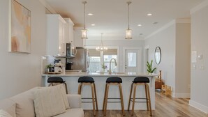 A modern kitchen with white cabinets, a central island with stools, and a dining area with a wooden table and chairs.