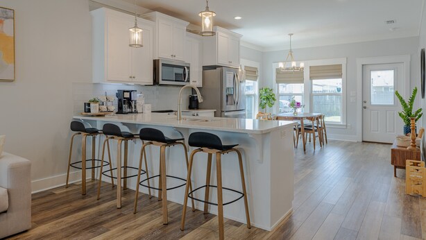 A modern kitchen with white cabinets, a central island with bar stools, stainless steel appliances, and pendant lighting.