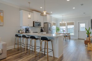 Une cuisine moderne avec des meubles blancs, un îlot central doté de tabourets, des appareils en acier inoxydable et un éclairage suspendu.