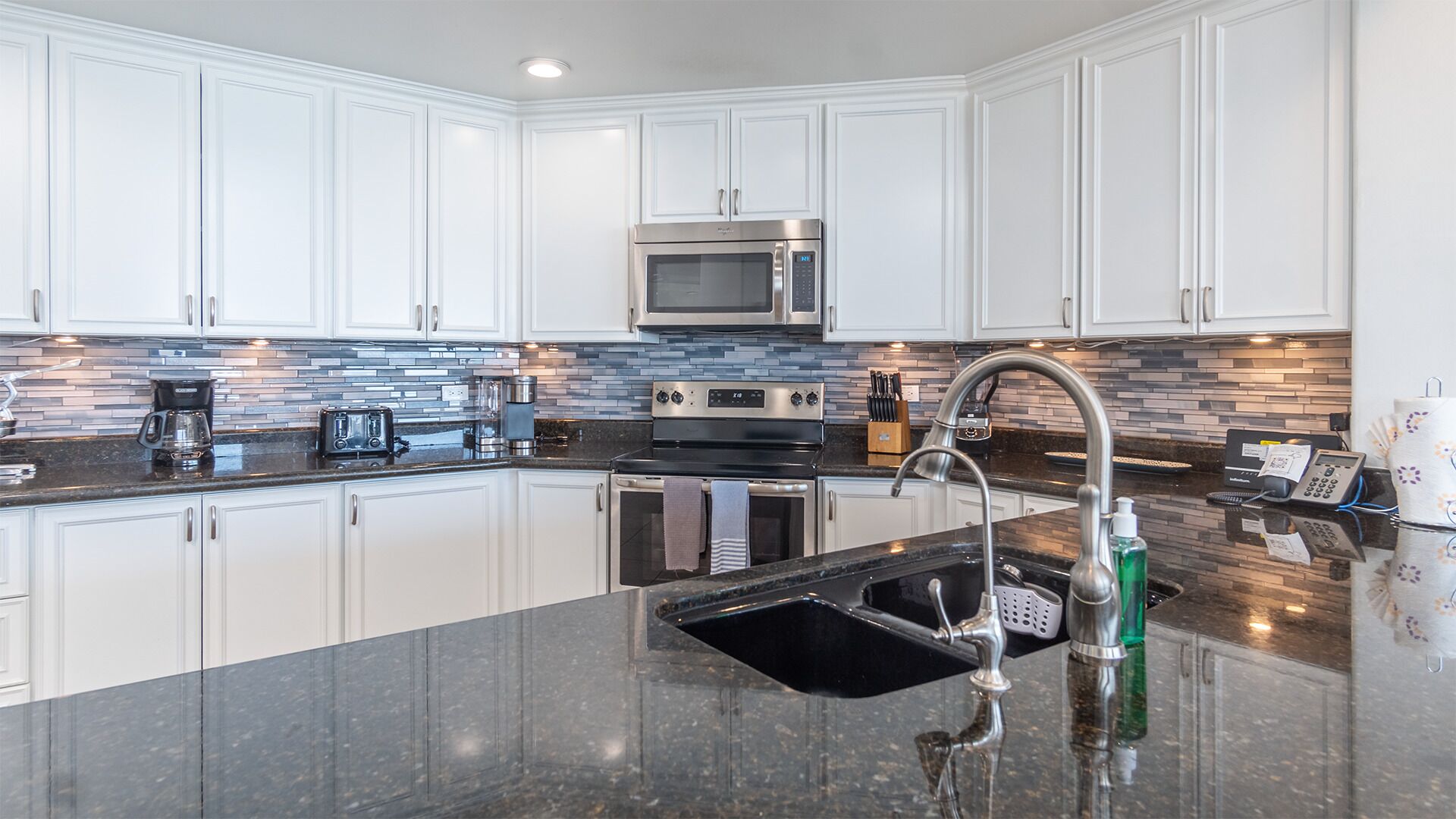 A modern kitchen with white cabinets, a stainless steel microwave, a double oven, and a granite countertop.