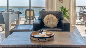 Una sala de estar moderna con un sofá de cuero, una mesa de centro de madera con unos binoculares y un cuenco, y vista al mar a través de grandes ventanales.