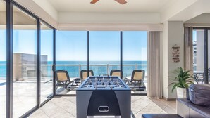 Una habitación con mesa de futbolín, un sofá y vista al océano.