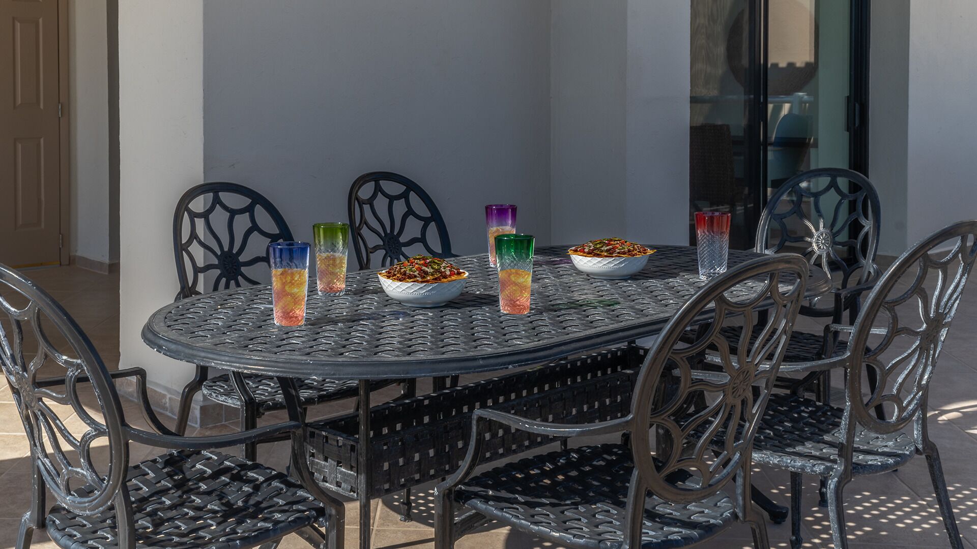 An outdoor dining area with a round metal table and chairs, surrounded by a white wall.