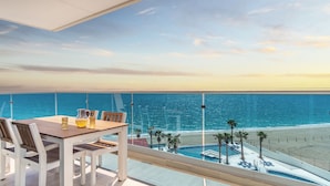 Ein Balkon mit Tisch und Stühlen, der auf einen Strand und den Ozean blickt.