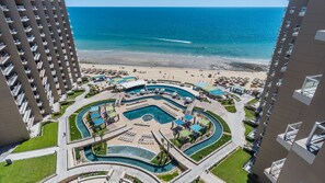 Ein Resort mit einem zentralen Poolbereich, mehreren Schwimmbecken und einem Strand.