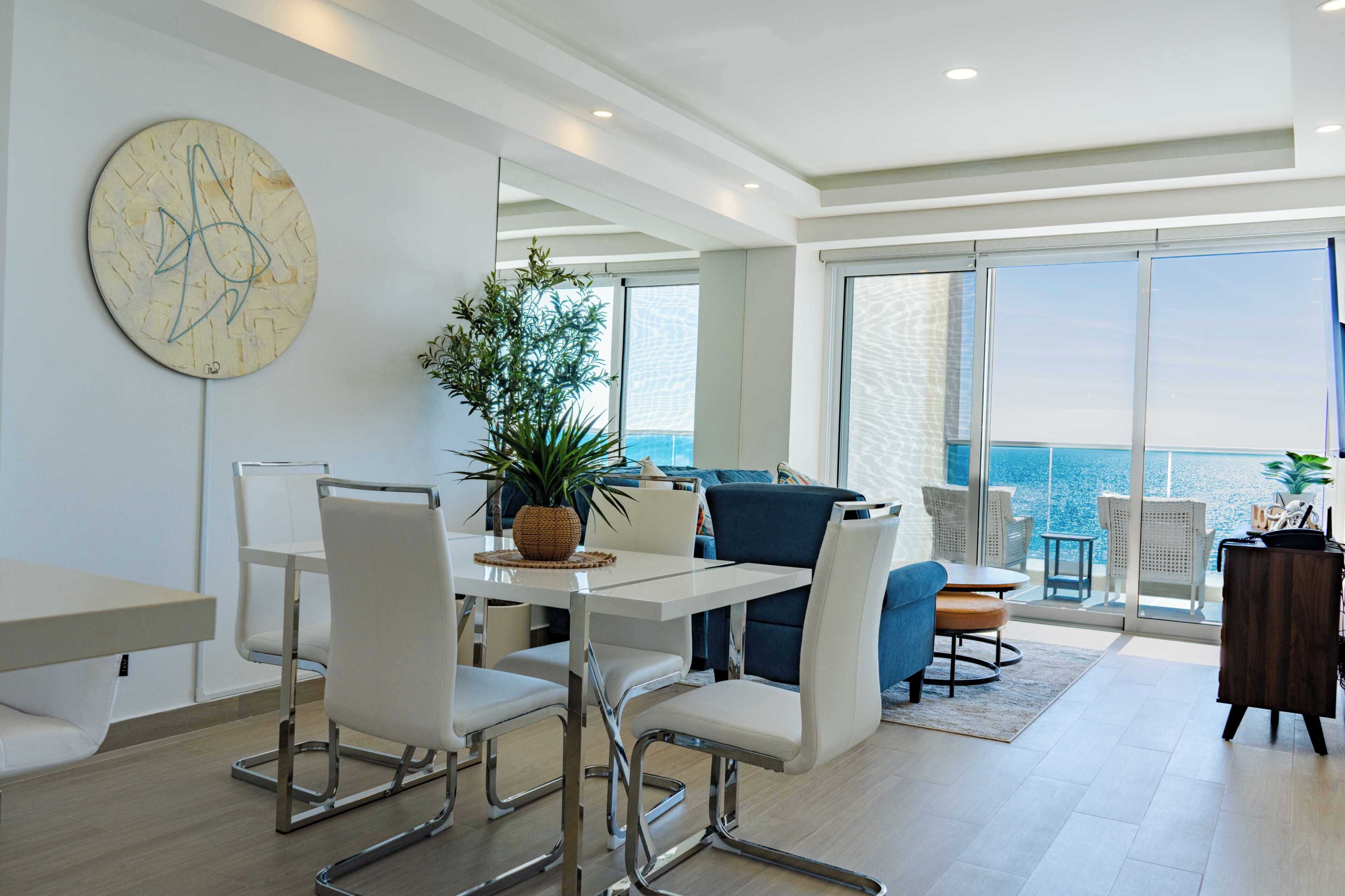 A modern living room with a dining area, large windows, and a view of the ocean.