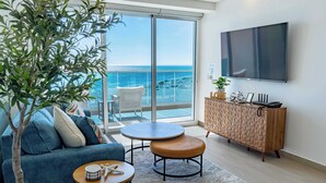 A modern living room with a sofa, two round tables, a TV, and a view of the ocean.