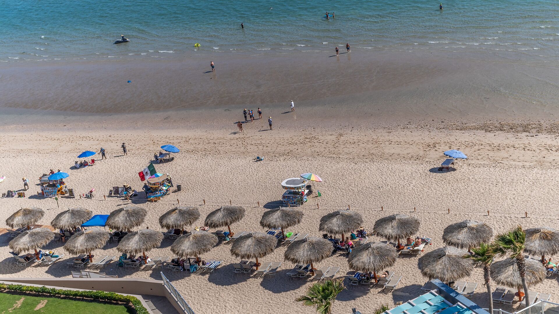 An aerial view of a beach with sun loungers, umbrellas, and a few people.