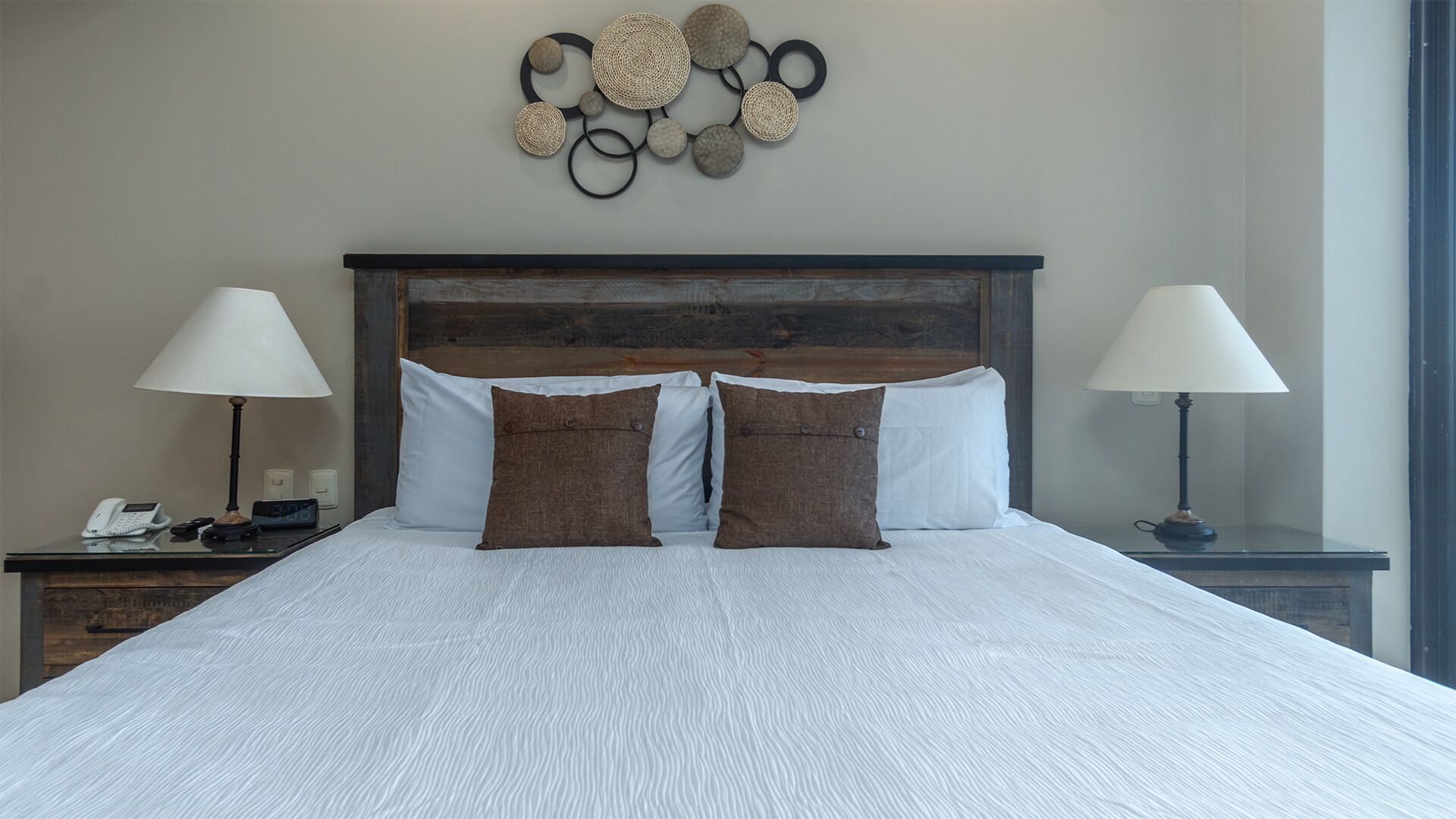 Een net opgemaakt bed met twee kussens, een decoratief object aan de muur en bedlampjes.