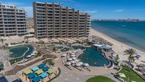 Ein Resort mit mehreren Swimmingpools, einem Strand und Hochhäusern im Hintergrund.