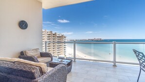 Ein Balkon mit Korbmöbeln, Blick auf den Strand und eine Stadtlandschaft im Hintergrund.