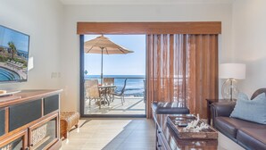 Une chambre d’hôtel moderne avec un balcon donnant sur la mer, une télévision à écran plat, un canapé et un coin repas avec une table et des chaises.
