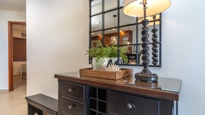 Une chambre moderne avec un bureau à plateau en verre, une commode en bois foncé dotée de tiroirs, un miroir et une lampe.