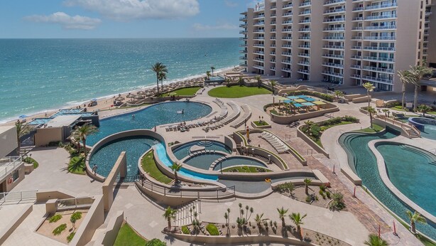 Un complexe h ôtelier doté de plusieurs piscines, d’une plage et d’un immeuble de grande hauteur.