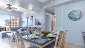 Un salon moderne comprenant un coin repas, une grande fenêtre donnant sur un immeuble de grande hauteur et un ventilateur de plafond.