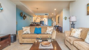 A spacious living room with a beige sofa set, a coffee table, and a dining area in the background. - Las Palomas 2 BR 2 BA Coronado 1204 (Puerto Peñasco)