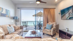A living room with a sofa, armchair, and coffee table, a balcony with a table and chairs, and a large window with a view of the sea. - Las Palomas 2 BR 2 BA Coronado 1204 (Puerto Peñasco)