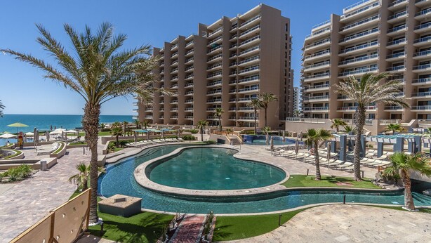 A resort with a large pool, palm trees, and a view of the ocean.