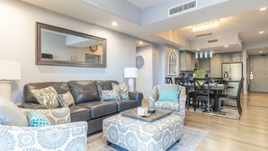 A modern living room with a leather sofa, patterned ottoman, and a dining area with a wooden table and chairs.
