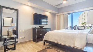 A modern hotel room with a large bed, a flat-screen TV, a dresser, and a view of tall buildings.