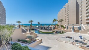 Um resort com piscina, palmeiras e vista para o oceano.