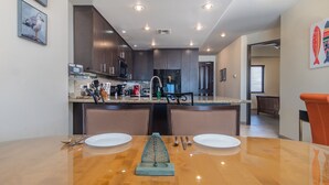 Una cocina moderna con armarios oscuros, encimera de granito y electrodomésticos de acero inoxidable. Cuenta con un comedor con una mesa de madera y dos sillas.