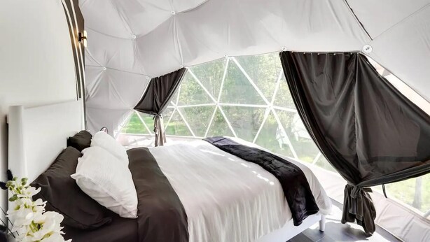 A tent-style room with a bed, white curtains, and a view of greenery outside. - 007 Geodome - Unique Escapes "007" Luxury Camping Geo-Dome! (Monticello)