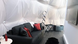A modern living room with a black sofa, red and black cushions, a white side table, a black furry rug, and a mirrored wall. - 007 Geodome - Unique Escapes "007" Luxury Camping Geo-Dome! (Monticello)