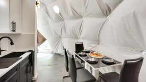 A modern kitchen with a unique geometric wall design, a dining area with a table set for two, and a black chair. - 007 Geodome - Unique Escapes "007" Luxury Camping Geo-Dome! (Monticello)