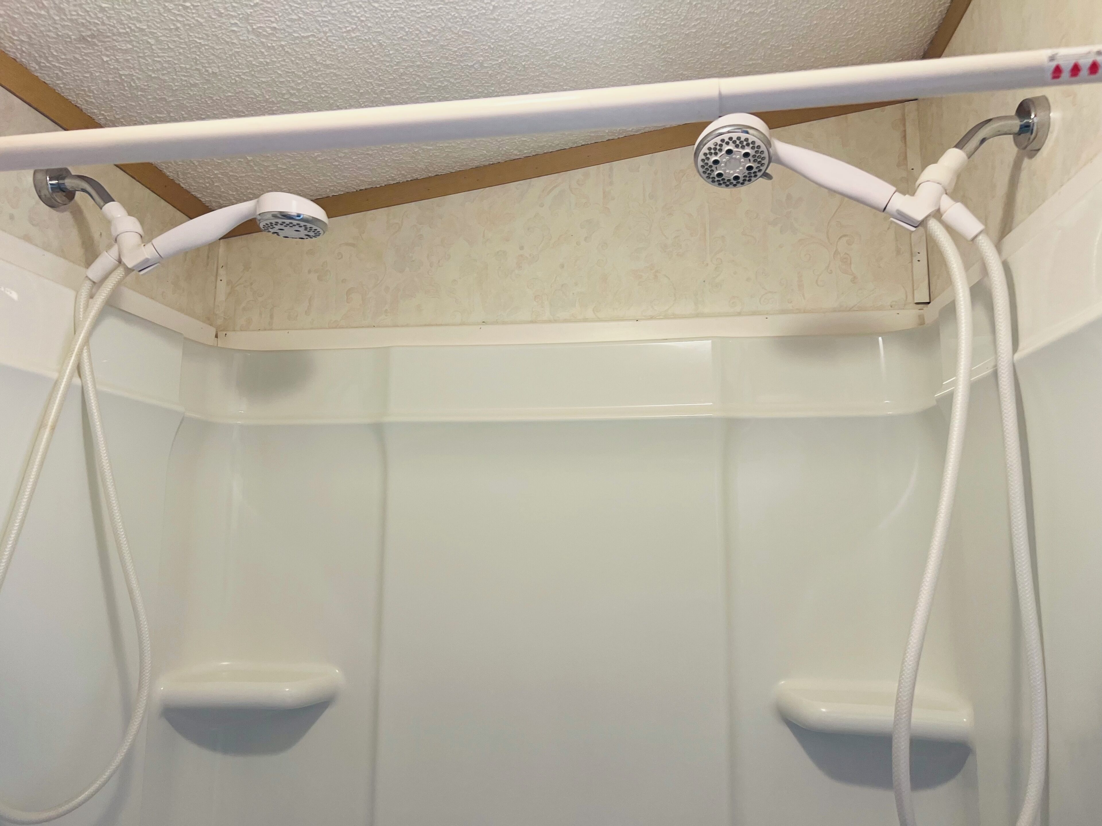 Une douche équipée de deux pommeaux de douche à main et d’un panneau de commande situé au-dessus.