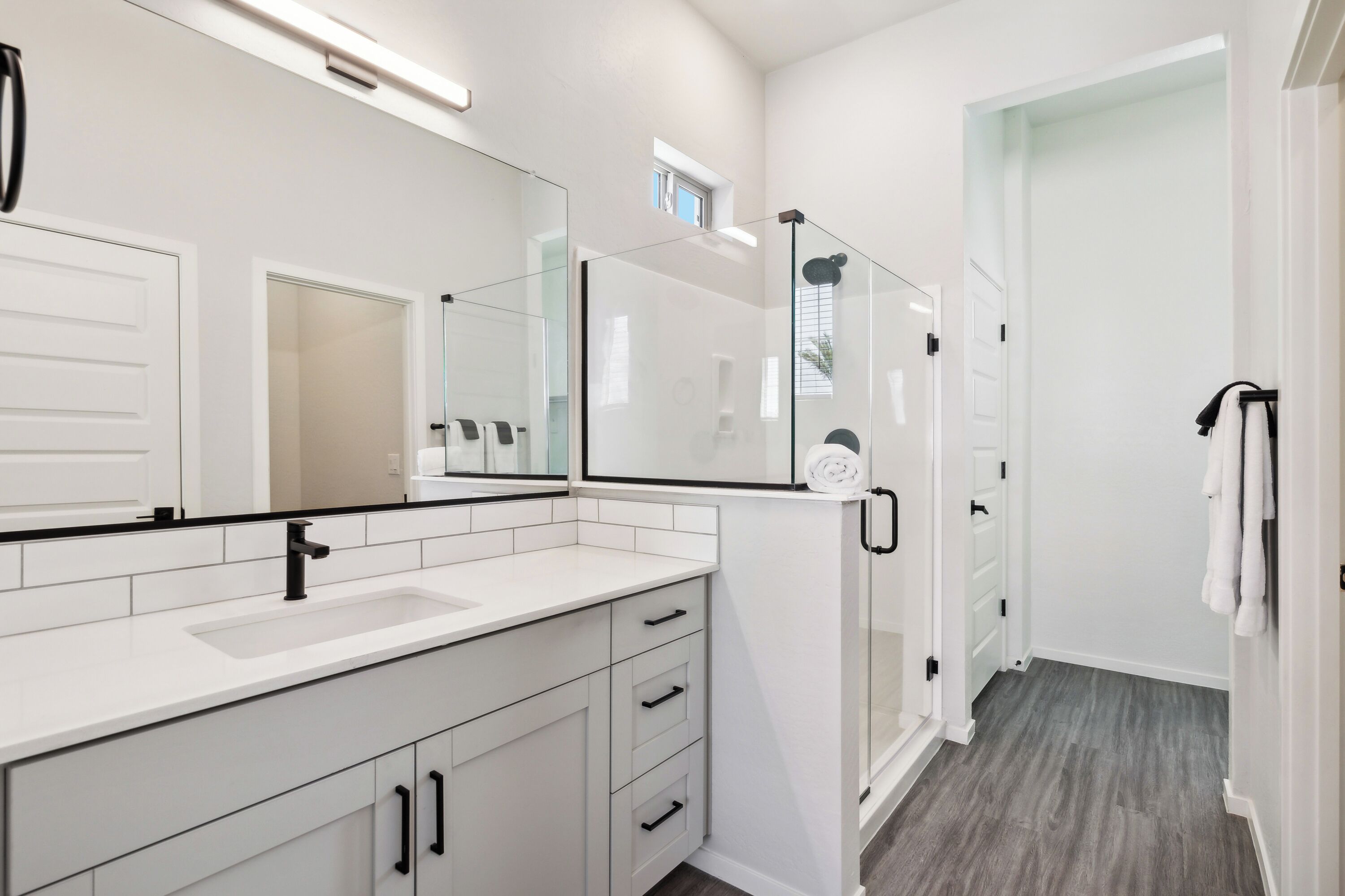 A modern bathroom with a large mirror, white cabinetry, a glass shower enclosure, and a walk-in shower.