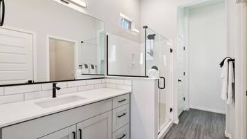 A modern bathroom with a large mirror, white cabinetry, a glass shower enclosure, and a walk-in shower.