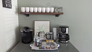 Een koffiehoek met een Keurig machine, een French press, een koffiezetapparaat en een dienblad met koffiecups en een mok.