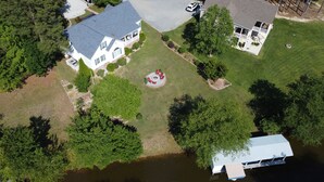 Luchtbeeld van een woongebied met huizen, een rond terras met rode stoelen en een steiger die in het water uitloopt.