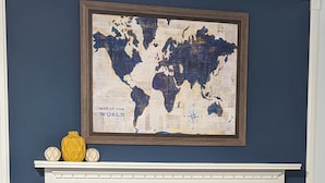 Een open haard met een stenen omlijsting, een wereldkaart erboven en decoratieve objecten op de schouw.