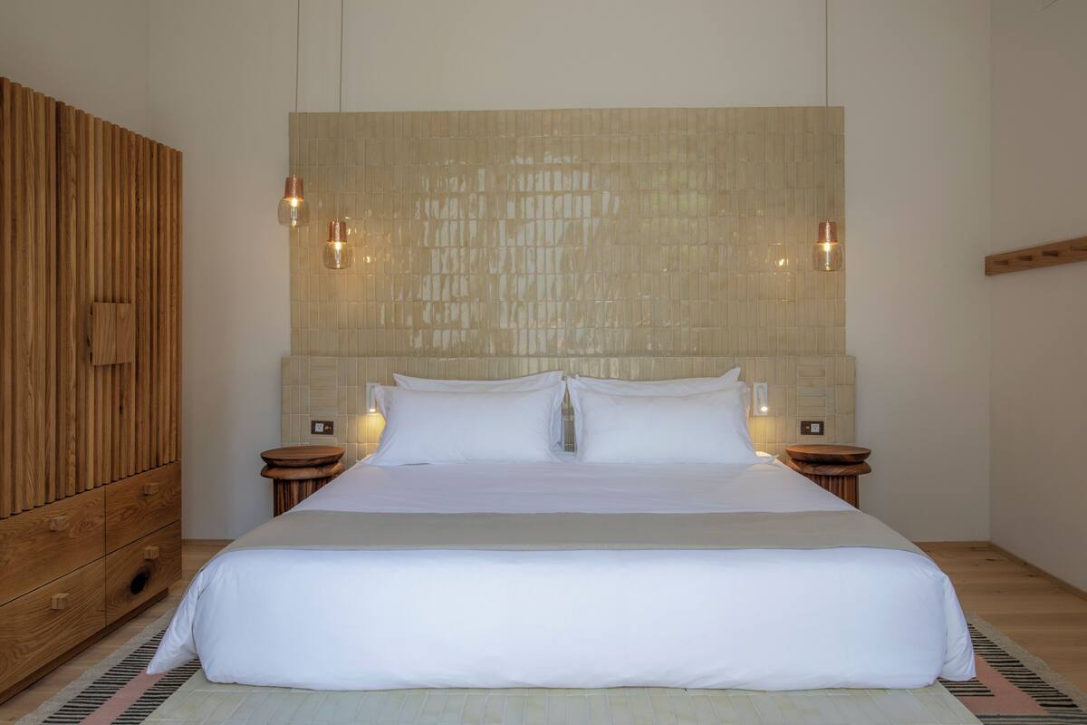 A large bed with white linens, a wooden headboard, and two bedside tables with lamps.