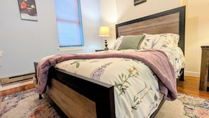 Un dormitorio con cama, mesita de noche, lámpara y ventana con persianas.