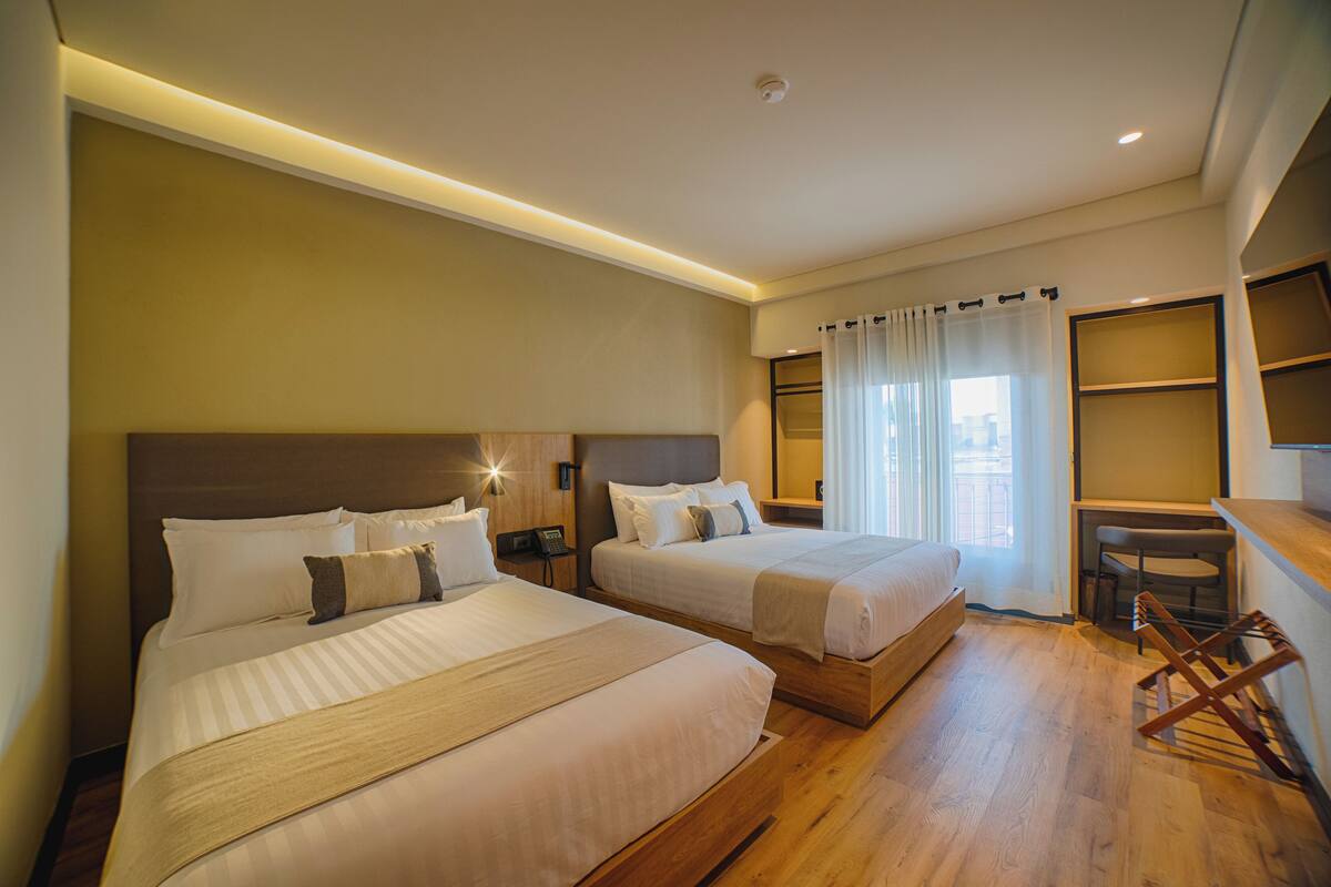 A hotel room with two beds, a desk, and a chair.