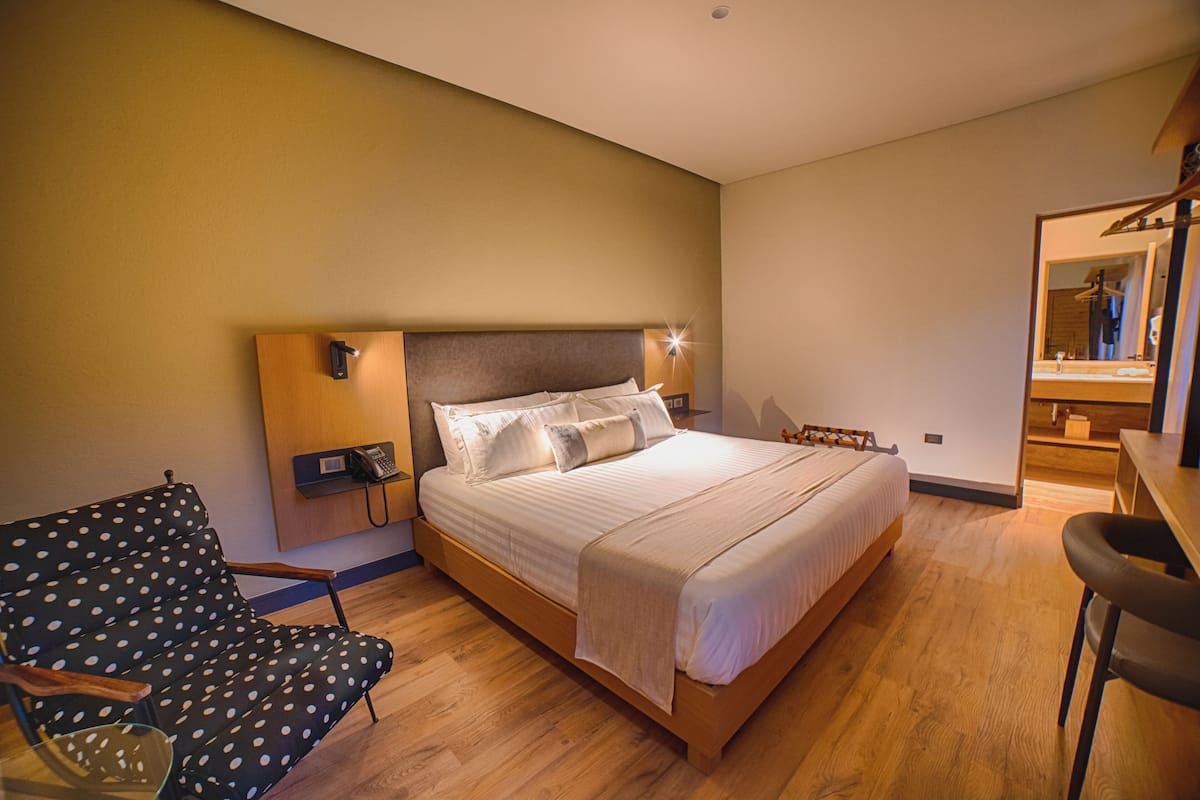 A hotel room with a bed, a chair, a desk, and a mirror.
