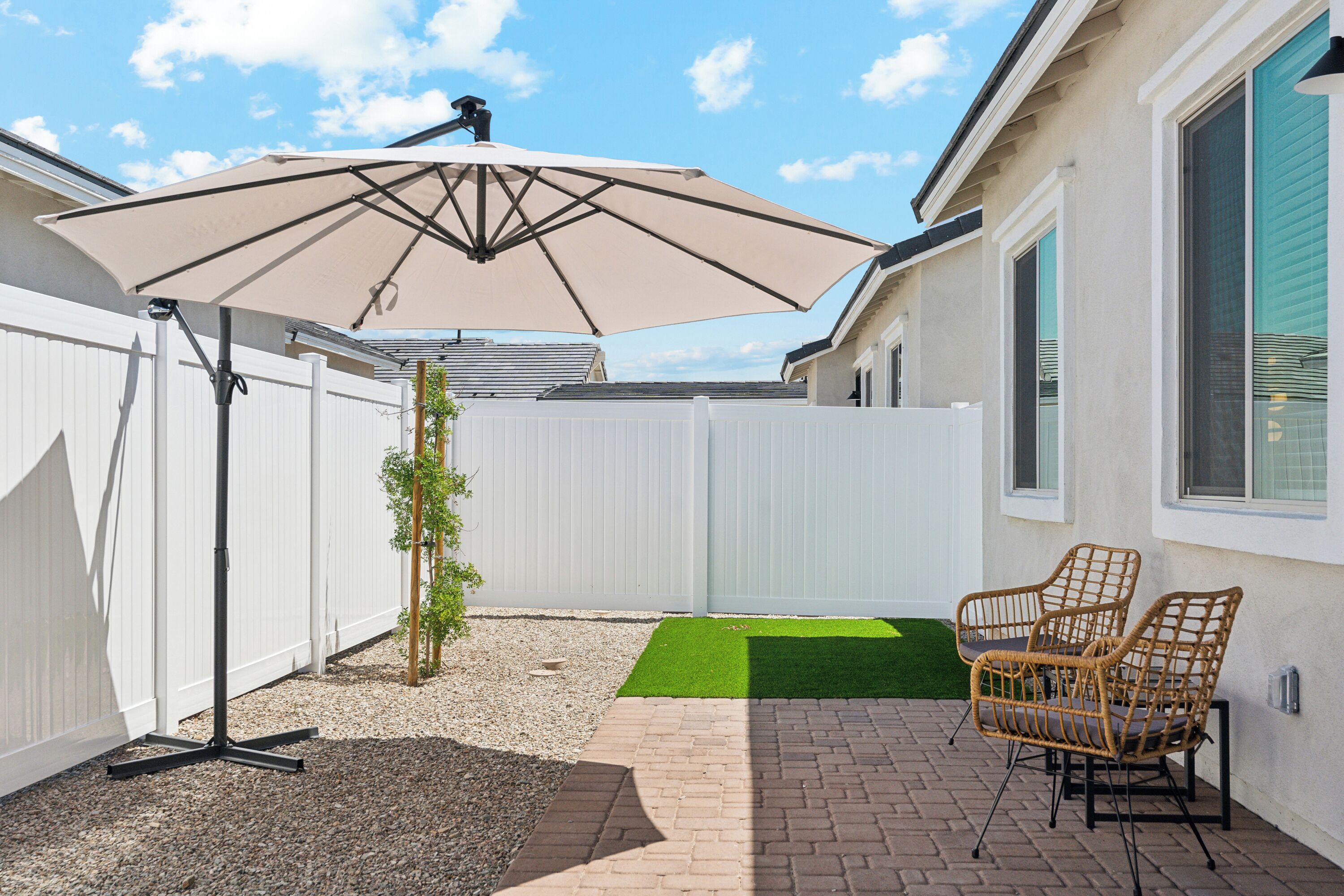 A patio area with a white fence, a beige umbrella, and wicker chairs.