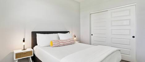 Un dormitorio ordenado con cama, mesita de noche, lámpara y una puerta cerrada.