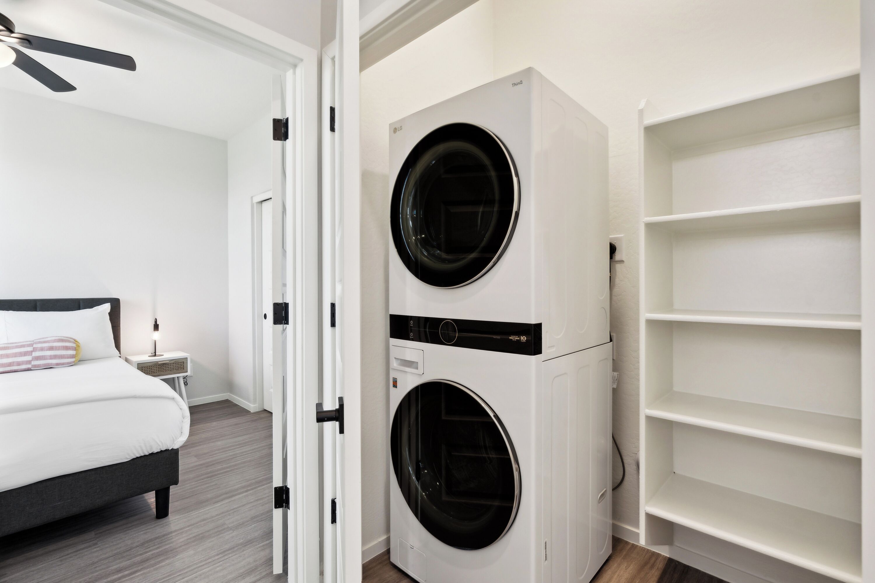 A bedroom with a bed, a wall-mounted washer and dryer, and a white shelving unit.